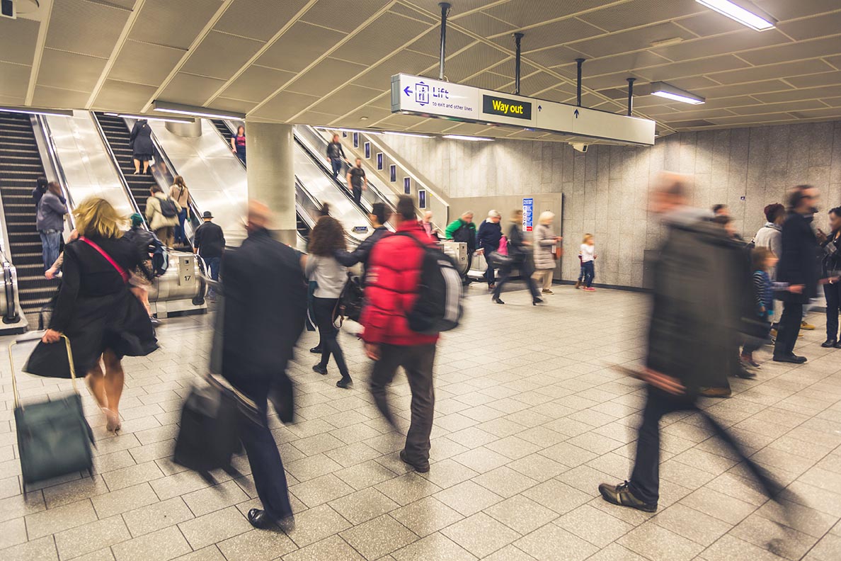 Blurred people walking inside train station or airport, with luggage and bags. There are some escalators on background, with people walking on both directions. Travel and urban lifestyle concepts.